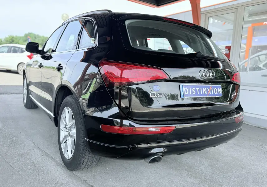 Audi Q5 noir vue 3/4 arrière droit, avec feux arrière rouges et sortie d’échappement visible.