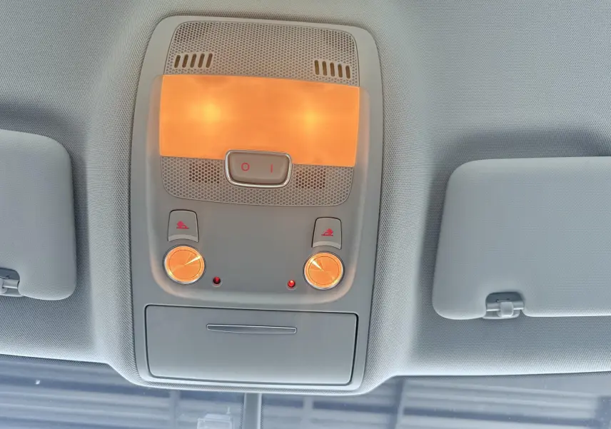 Plafonnier intérieur allumé vu de dessous dans un Audi Q5 noir, avec deux boutons et deux lampes rondes orangées.