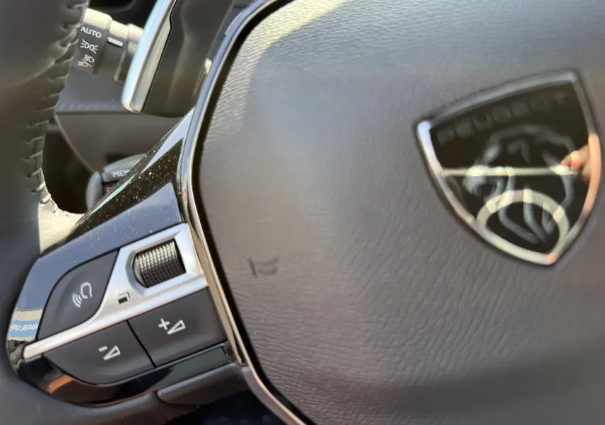 Gros plan sur le volant en cuir noir du Peugeot 2008 Hybrid 145ch Allure, avec commandes intégrées et logo lion chromé.