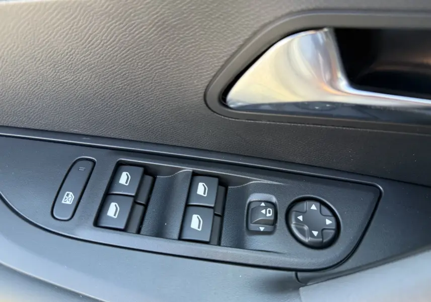 Gros plan sur les commandes de lève-vitres et réglage des rétroviseurs côté conducteur d'une Peugeot 2008 gris selenium.