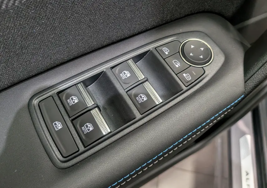 Gros plan sur les commandes de lève-vitres et rétroviseurs côté conducteur, avec surpiqûres bleues sur le panneau noir.