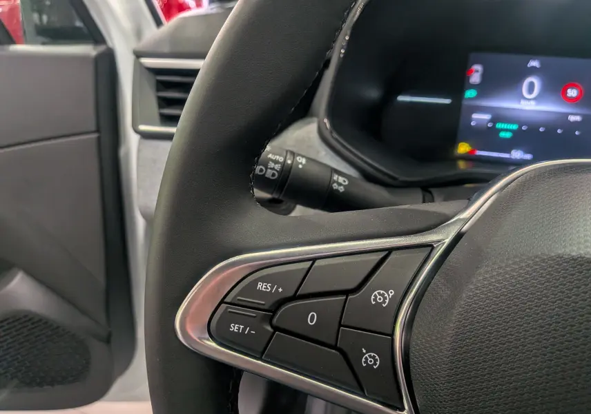 Gros plan sur le volant noir de la Renault Clio V blanc glacier, montrant les commandes de régulateur de vitesse côté gauche.