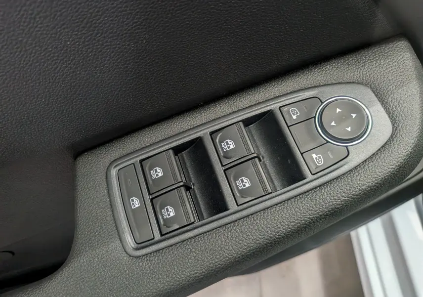 Gros plan sur les commandes électriques des vitres et rétroviseurs sur la porte intérieure côté conducteur d'une Renault Clio V.