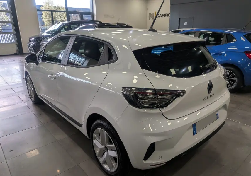 Vue 3/4 arrière droite d'une Renault Clio V Blanc Glacier 2025 en intérieur, avec feux arrière LED et jantes alliage.