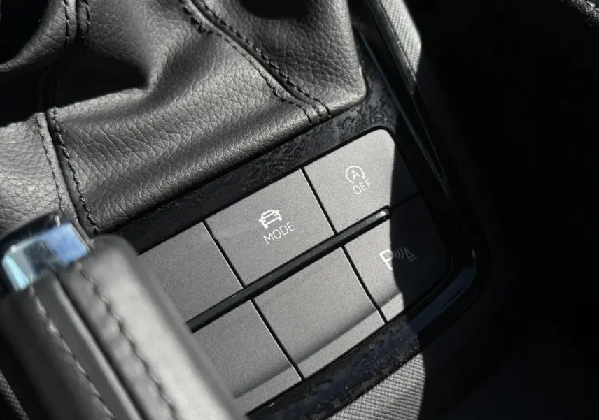 Gros plan sur les boutons de commande gris mat près du levier de vitesse en cuir noir dans une Skoda Scala Bleu Energy.