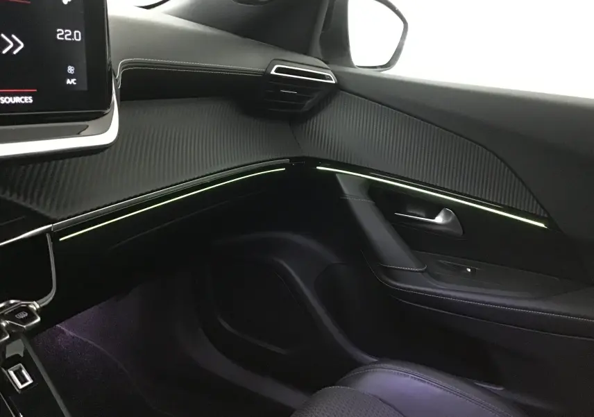 Intérieur côté passager du Peugeot 2008 blanc nacré, mettant en valeur la planche de bord noire avec éclairage d'ambiance subtil.