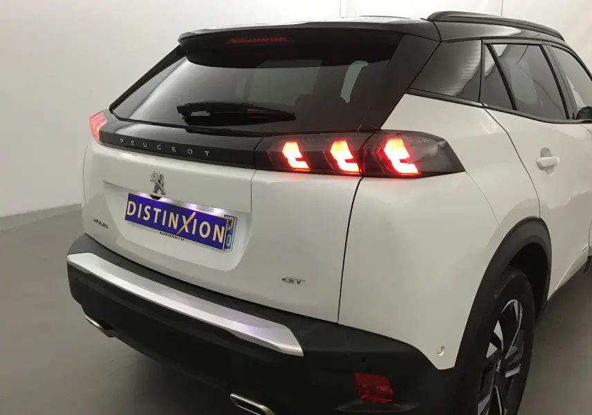 Vue 3/4 arrière droite du Peugeot 2008 GT blanc nacré avec feux arrière allumés et toit noir contrasté.