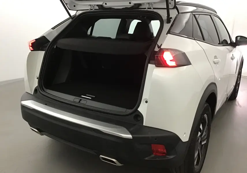 Vue arrière droite du Peugeot 2008 blanc nacré avec coffre ouvert et feux arrière allumés dans un intérieur neutre.