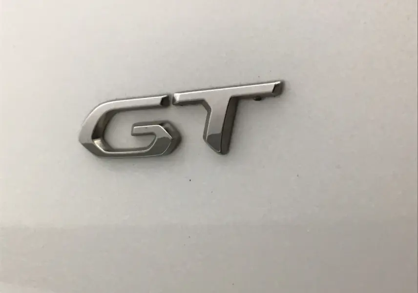 Gros plan sur l'emblème GT chromé sur la carrosserie blanc nacré d'un Peugeot 2008 GT 2021.