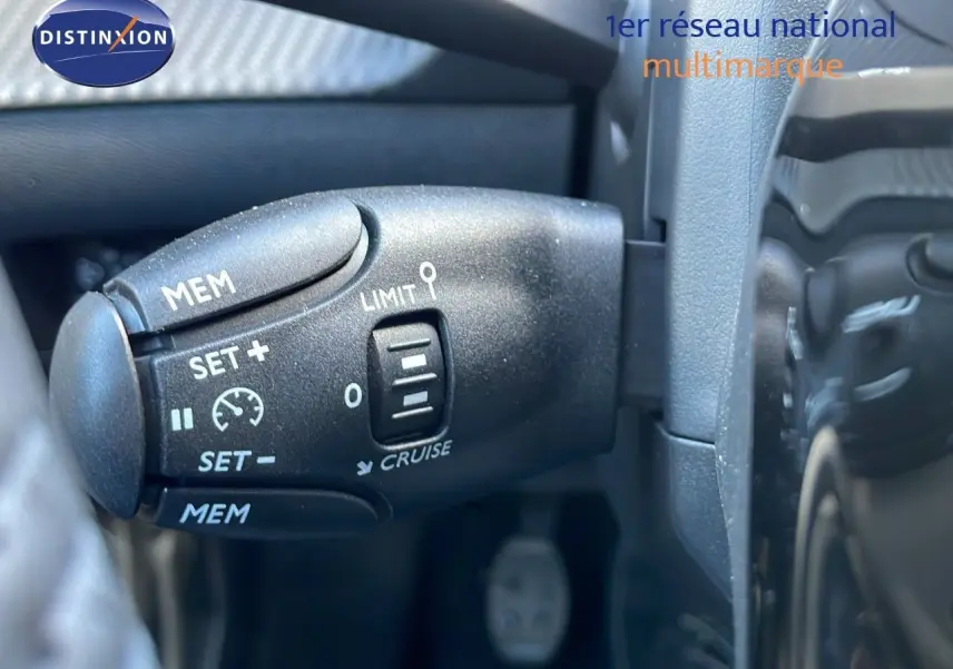 Gros plan sur la commande de régulateur de vitesse à gauche du volant dans le Peugeot 2008 rouge Elixir Metal 2025.