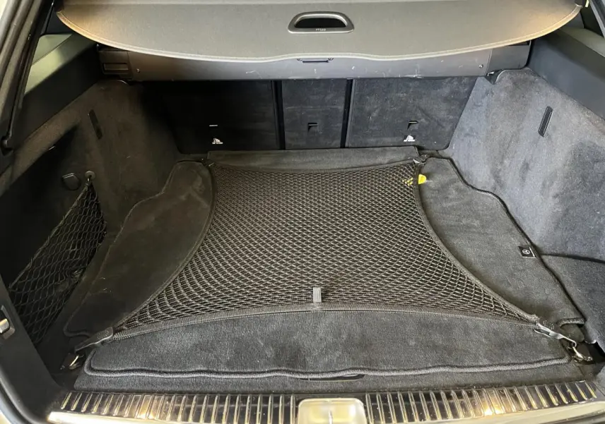 Coffre ouvert d'un Mercedes Classe C Break blanc, vue intérieure avec filet de rangement noir et tapis de sol.