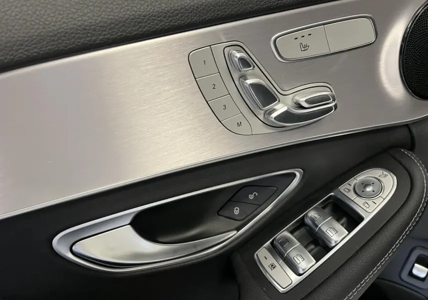 Détail de la porte côté conducteur d'une Mercedes Classe C Break blanc, avec commandes sièges et vitres en finition aluminium brossé.