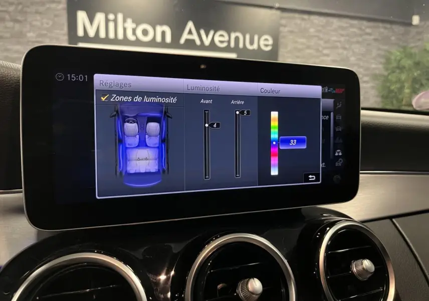 Écran central du tableau de bord d'une Mercedes Classe C Break blanc, réglage de l'éclairage intérieur en bleu visible.