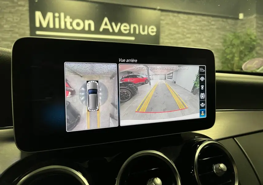 Écran multimédia montrant la caméra de recul et vue 360° d'un break Mercedes Classe C blanc, intérieur noir.