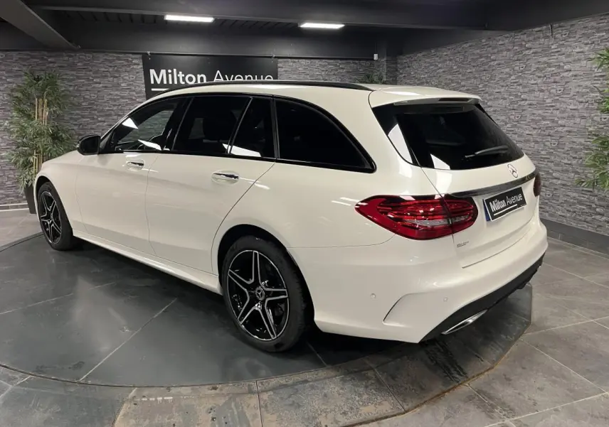 Vue 3/4 arrière côté gauche d'un break Mercedes Classe C blanc avec jantes AMG noires et vitres teintées.