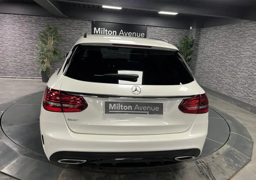 Vue arrière d'un break Mercedes Classe C blanc avec feux LED et double sortie d'échappement chromée dans un showroom.