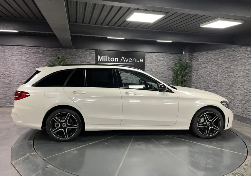 Mercedes Classe C Break blanc vue de profil côté gauche avec jantes AMG noires et argentées dans un showroom.