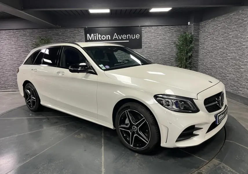 Mercedes Classe C Break blanc en 3/4 avant droit avec jantes AMG noires et toit ouvrant visible en intérieur showroom.