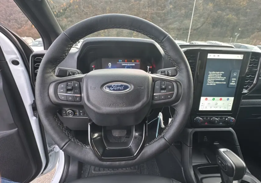 Vue intérieure centrée sur le volant cuir multifonctions d'un Ford Ranger blanc glacier avec écran tactile vertical.