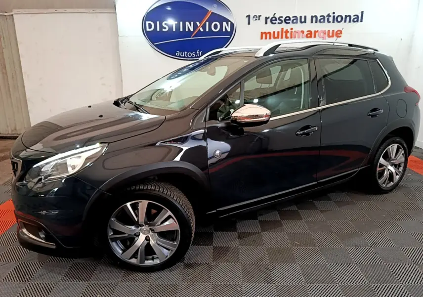 Peugeot 2008 gris foncé vue de profil côté gauche avec jantes alliage et barres de toit chromées.