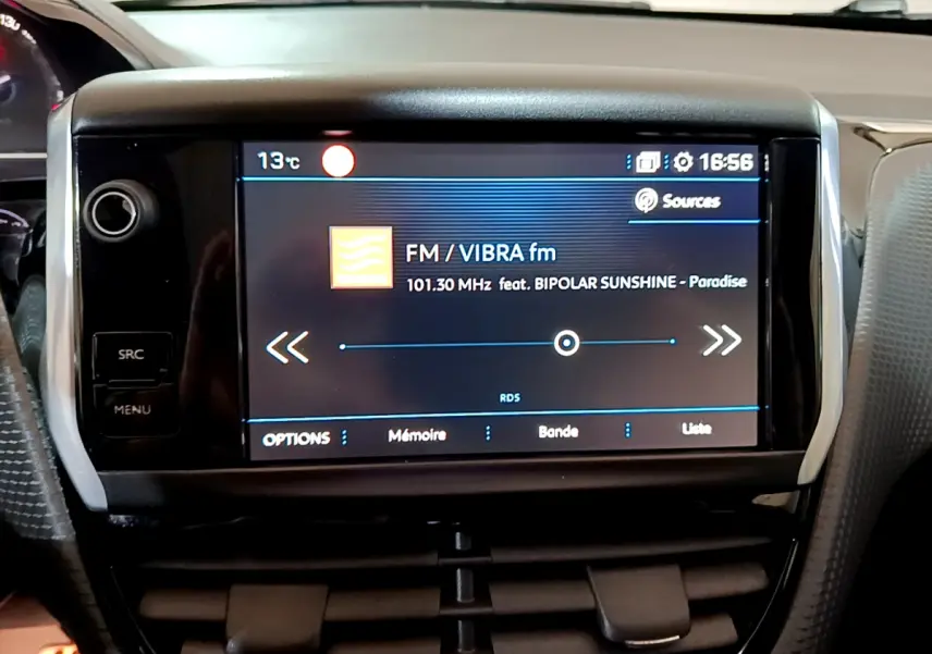 Écran tactile central affichant la radio FM dans l’habitacle d’une Peugeot 2008 gris foncé, vue de face rapprochée.