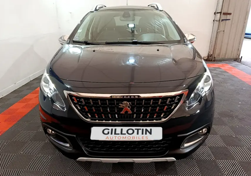 Vue avant d'un Peugeot 2008 gris foncé avec calandre chromée et phares allumés dans un garage.