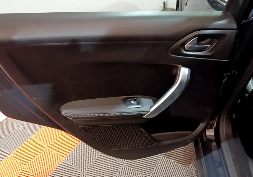 Gros plan sur la porte intérieure côté droit d'un Peugeot 2008 gris foncé, avec poignée argentée et commande de vitre.