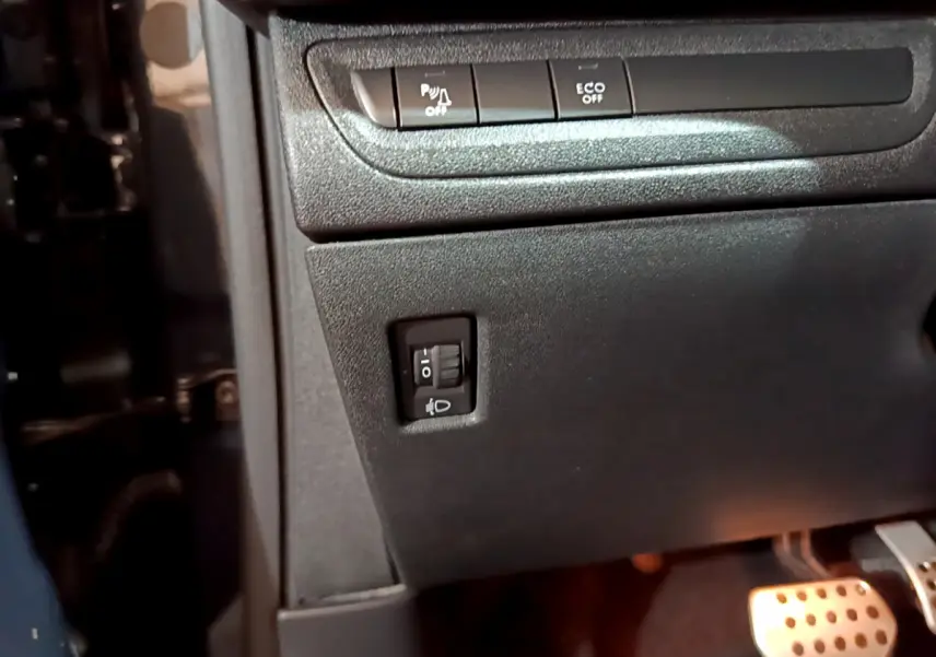 Détail du tableau de bord côté gauche avec boutons de réglage des phares et pédales en aluminium du Peugeot 2008 gris foncé.