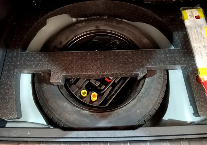 Vue plongeante sur la roue de secours noire et les outils de bord dans le coffre d'un Peugeot 2008 gris foncé.