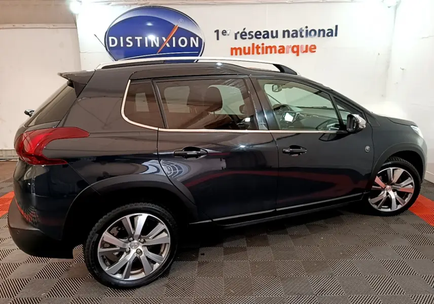 Peugeot 2008 gris foncé vue de profil côté gauche, avec jantes alliage et barres de toit chromées.