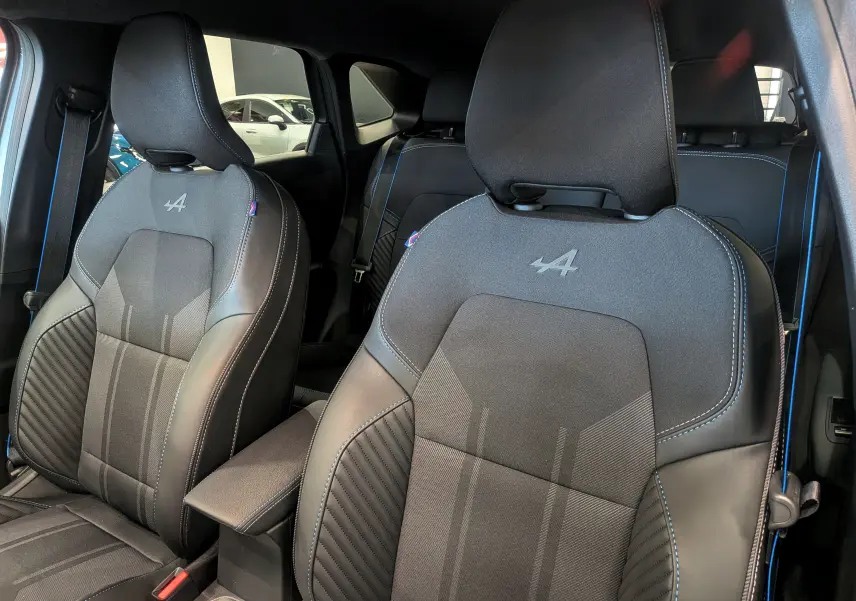 Vue intérieure rapprochée des sièges avant noirs avec surpiqûres bleues et logo Alpine sur un Renault Symbioz hybride 2026.