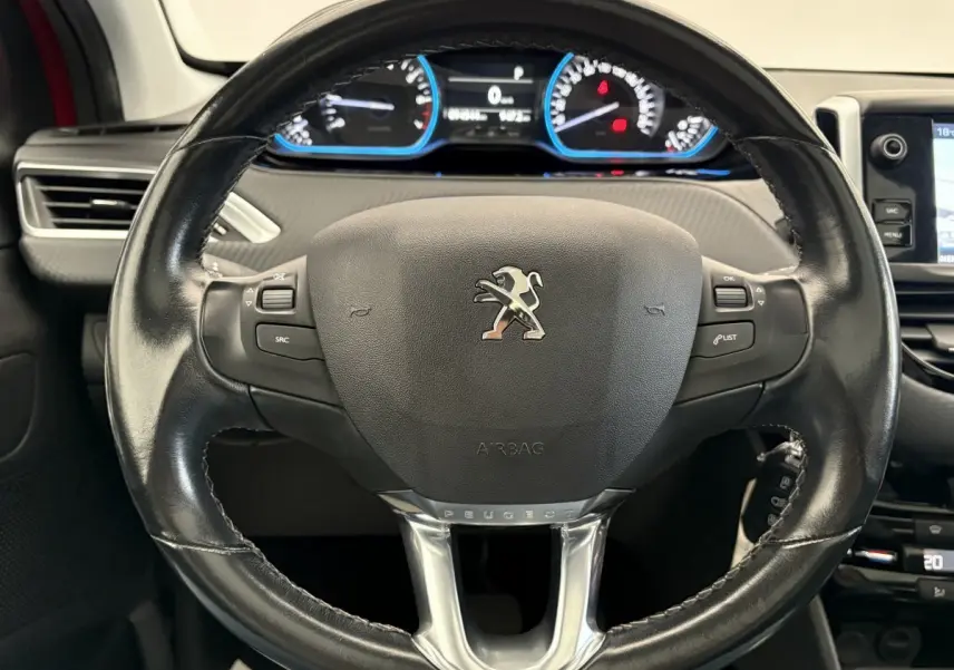 Gros plan sur le volant cuir noir du Peugeot 2008 rouge, avec tableau de bord numérique et commandes intégrées.