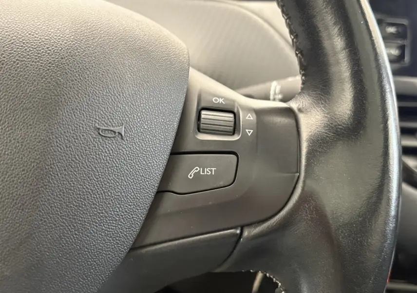 Gros plan sur le volant cuir noir de la Peugeot 2008 Puretech 110, avec commandes multifonctions côté droit.