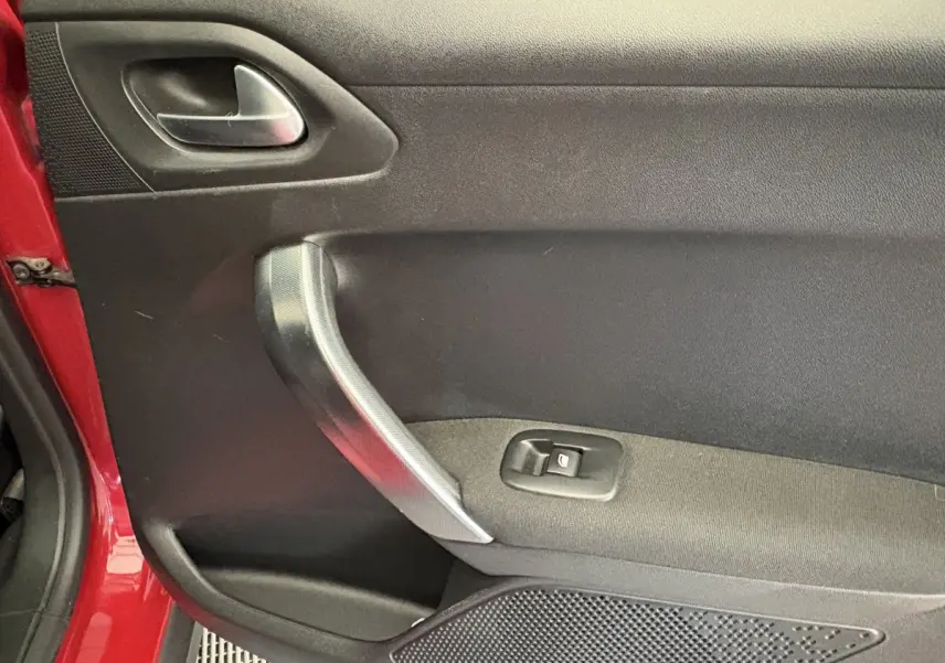 Gros plan sur la porte intérieure côté gauche d'une Peugeot 2008 rouge, avec poignée argentée et bouton de vitre électrique.