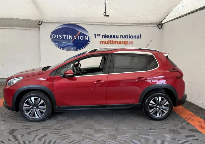 Profil droit d'un Peugeot 2008 rouge 2019 avec barres de toit chromées et jantes alliage dans un showroom.