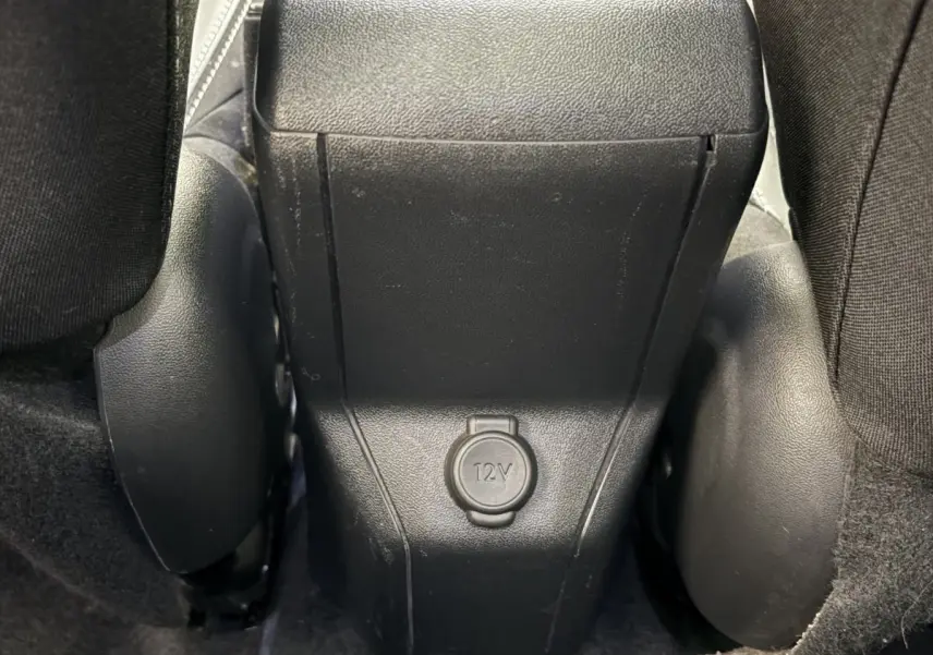 Prise 12V en gros plan entre les sièges arrière noirs d'une Peugeot 2008 rouge, version Puretech 110 S&S EAT6 Allure.