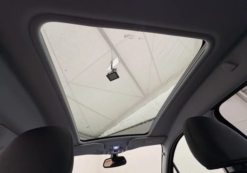 Toit panoramique ouvert vu de l'intérieur avant du Peugeot 2008 rouge, montrant les sièges avant et le rétroviseur central.