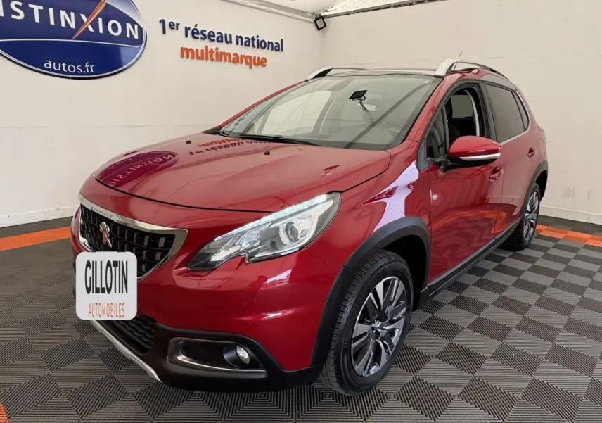 Peugeot 2008 rouge vue 3/4 avant droit, avec phares LED et barres de toit chromées en intérieur showroom.