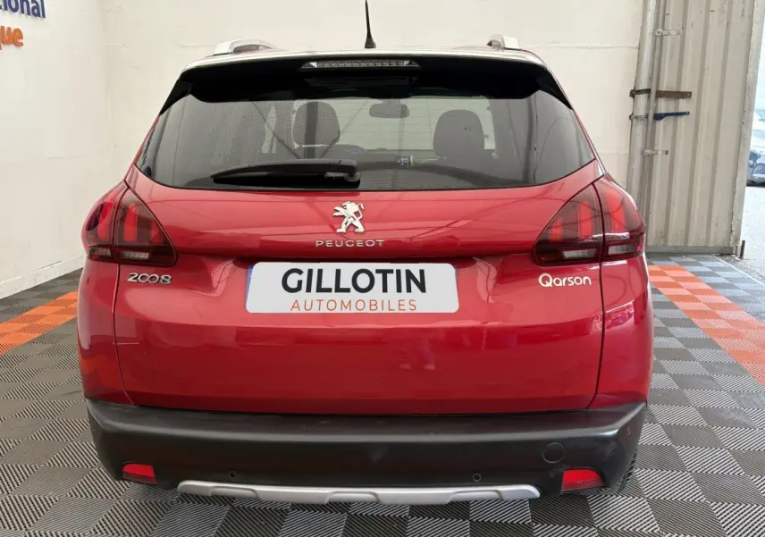 Vue arrière d'un Peugeot 2008 rouge avec logo et feux arrière distinctifs, stationné en intérieur sur sol damier.