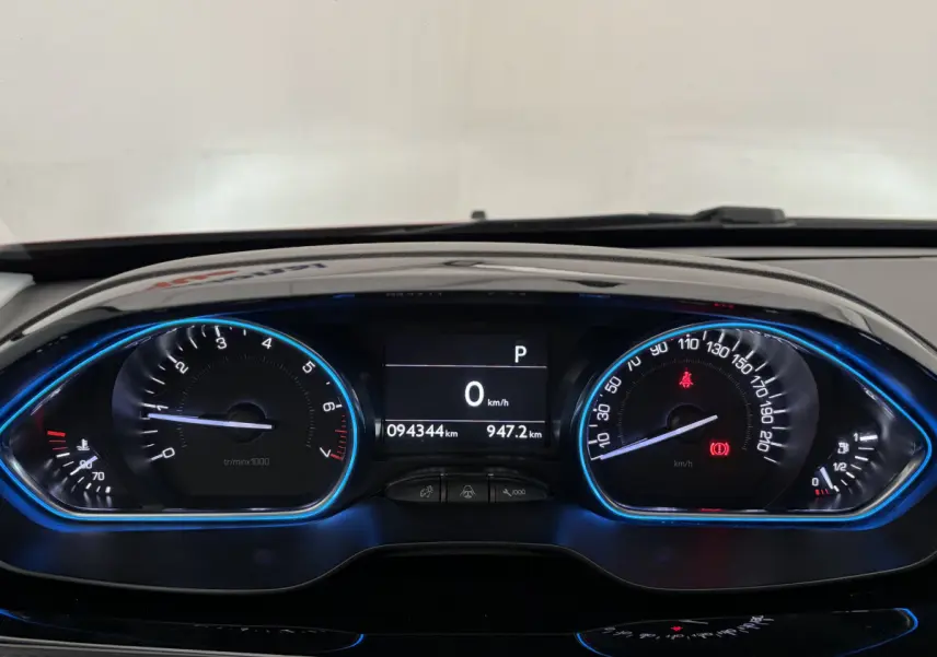 Tableau de bord numérique bleu de Peugeot 2008 rouge, affichant compteur et vitesse à 0 km/h en vue frontale.