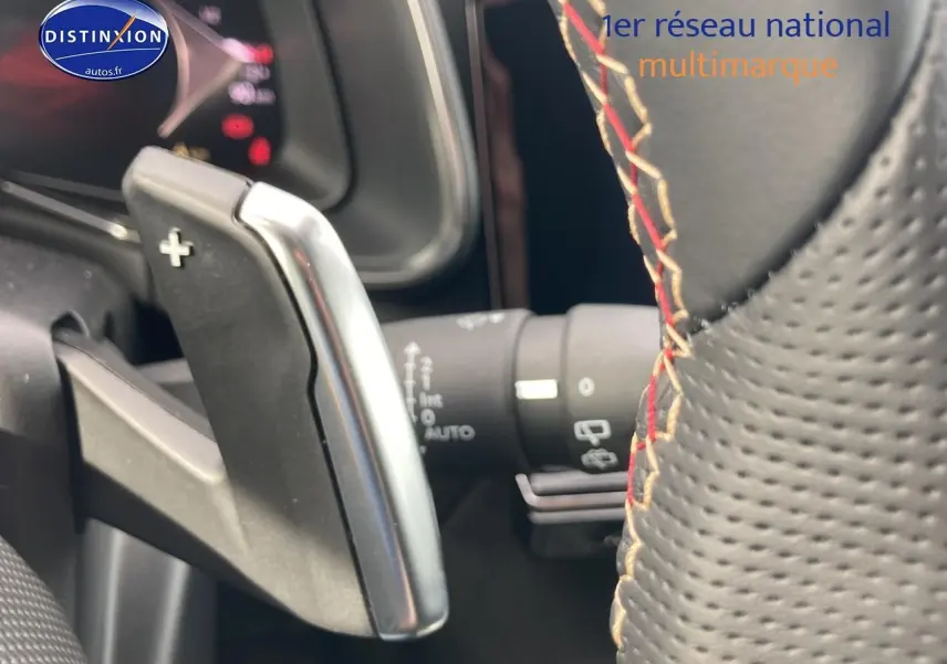 Gros plan sur la palette de changement de vitesse côté droit du volant en cuir perforé avec surpiqûres rouges du DS7 Crystal Pearl.