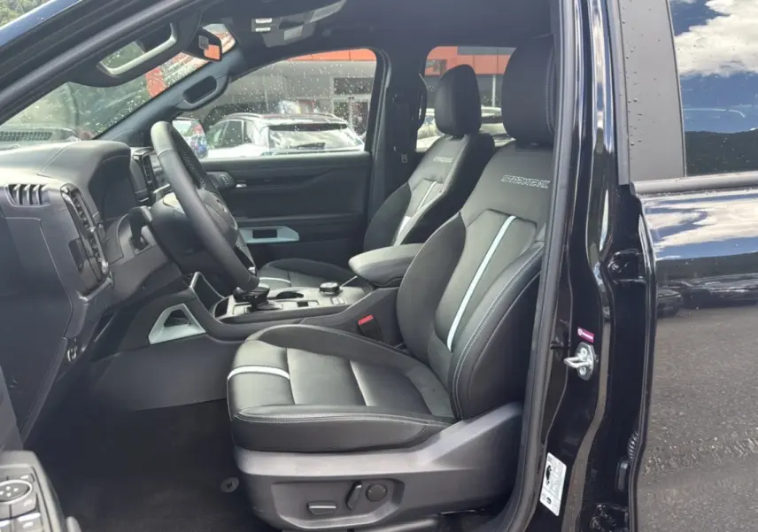 Vue intérieure côté conducteur du Ford Ranger noir agate 2025, sièges Stormtrak avec surpiqûres et volant cuir multifonctions.