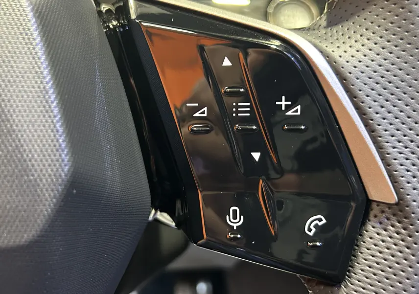 Gros plan sur les commandes noires brillantes du volant côté gauche du Peugeot 3008 gris Artense, avec boutons multifonctions.