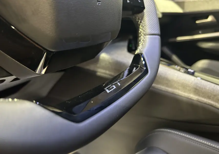 Gros plan sur le volant cuir noir avec logo GT du Peugeot 3008 III Hybrid, intérieur moderne et soigné.