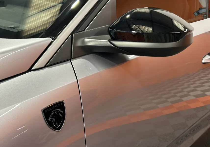 Détail du côté gauche d’un Peugeot 3008 gris Artense avec rétroviseur noir brillant et logo Peugeot noir.