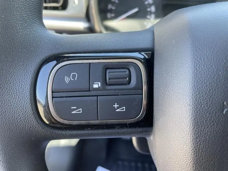 Gros plan sur les commandes de volume et de reconnaissance vocale sur le volant d'une Citroën C3 gris foncé 2019 version 82 CV Feel.