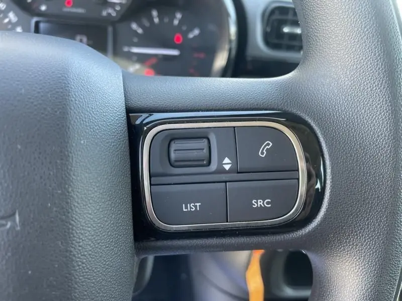 Gros plan sur les commandes du volant d'une Citroën C3 2019 gris foncé, boutons pour téléphone et liste audio visibles.