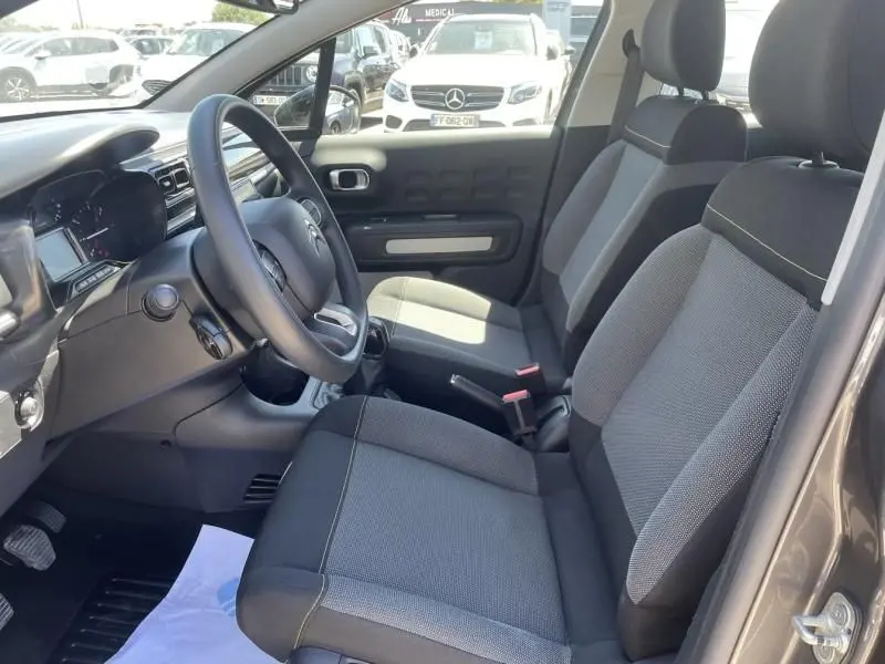 Intérieur avant côté conducteur d'une Citroën C3 2019 gris foncé métal, sièges tissu bicolore et volant multifonction.