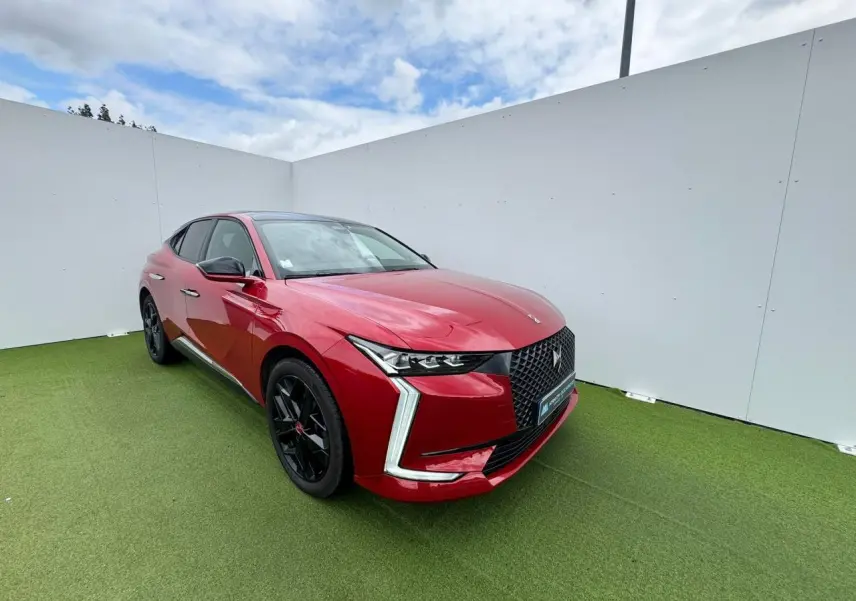 Vue 3/4 avant d'une DS4 rouge foncé avec calandre noire et jantes alliage noires sur fond vert gazon.