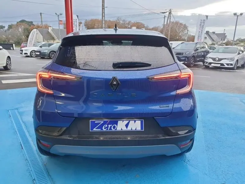 Vue arrière d'un Renault Captur 2025 bleu Iron avec feux arrière LED allumés sur parking.